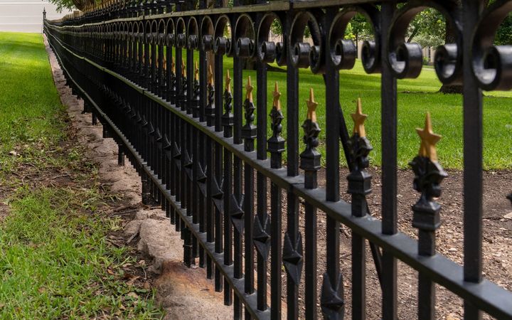 Black metal fence with gold finials along a lawn