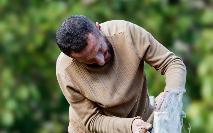 Man working on a fence post by hand, trees behind