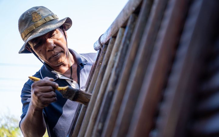 Man in a sun hat brushing stain onto wood fence boards