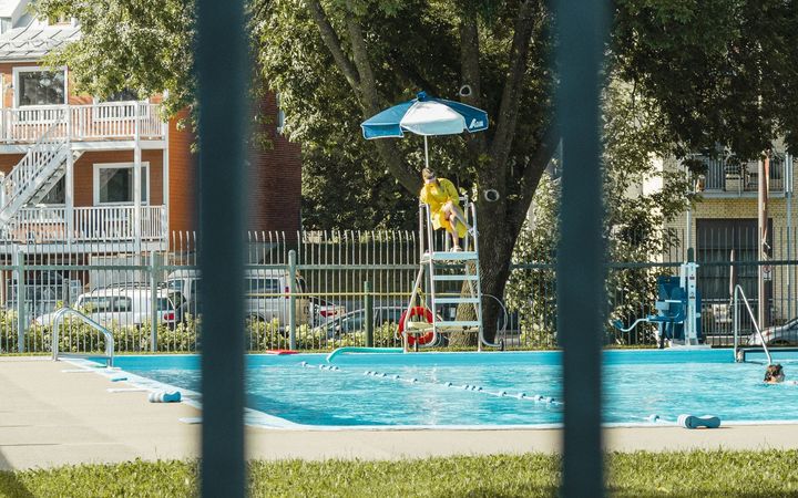 Outdoor swimming pool with a lifeguard chair, seen through fence bars