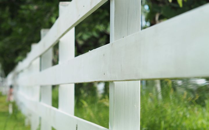 White three-rail fence running along a grass lawn